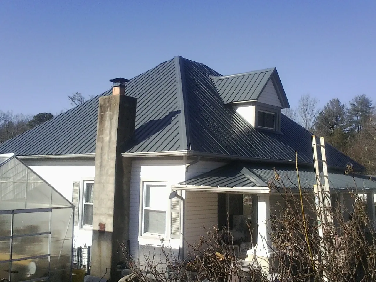 Dark blue standing seam metal roof on a white farmhouse with dormer — Slate & Tile Roof Repair by Roofing Brothers in Grand Ledge