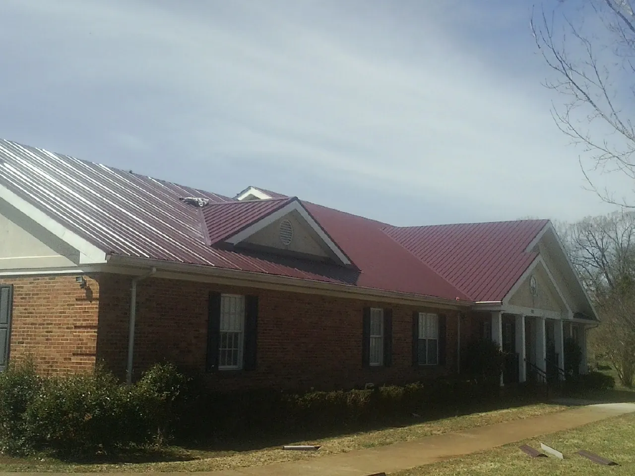 Red metal roof with gabled entries on a long brick building, from a Hail Damage Roof Repair job in Grand Ledge