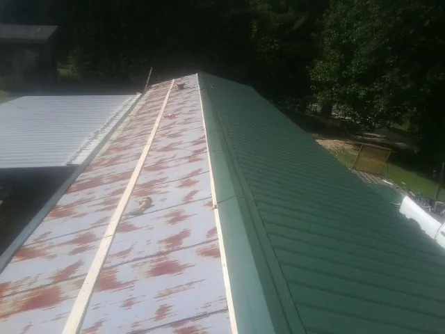 Old rusted panels beside newly installed green metal roofing — Wind Damage Roof Repair by Roofing Brothers in Grand Ledge