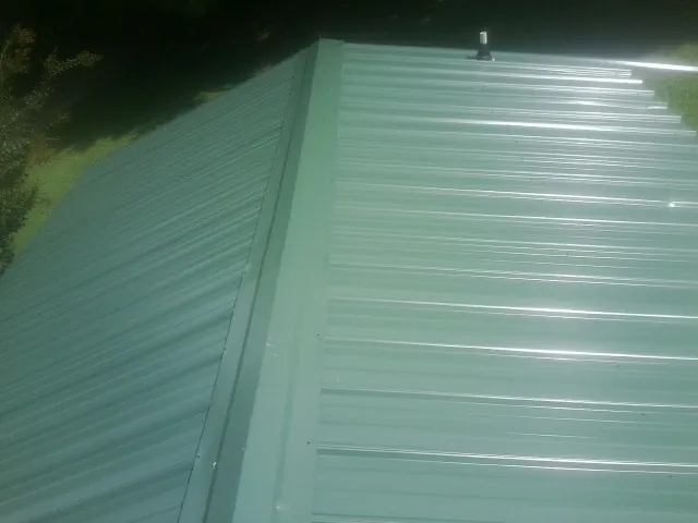 New green metal panels meeting at the ridge of a roof — Flat Roof Repair work by our crew in Grand Ledge