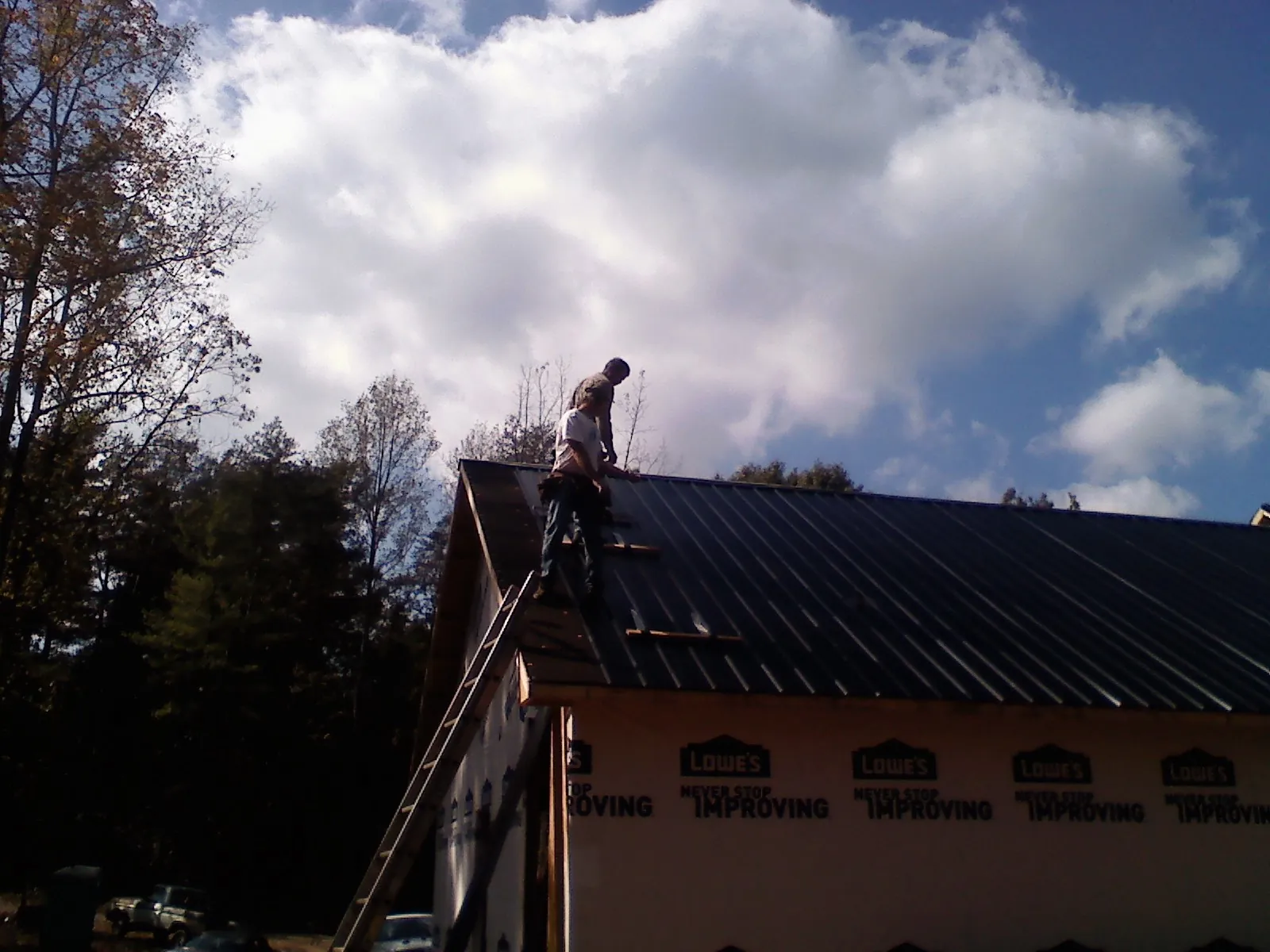 Roofer fastening dark metal panels high against a cloudy sky, from a Roof Inspection job in Grand Ledge