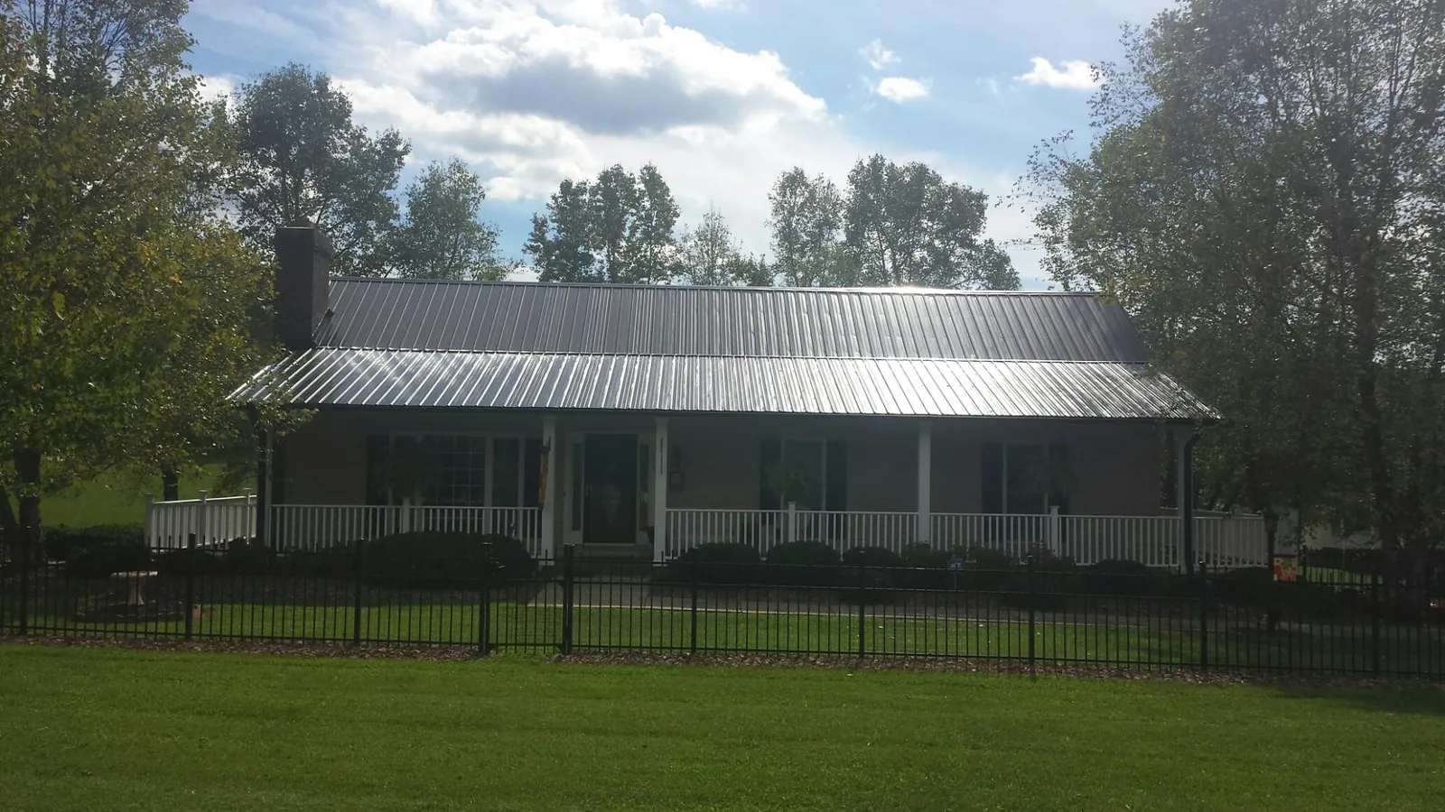 Gray metal roof on a brick ranch with a full width front porch — Gutter Guard Installation work by our crew in Grand Ledge