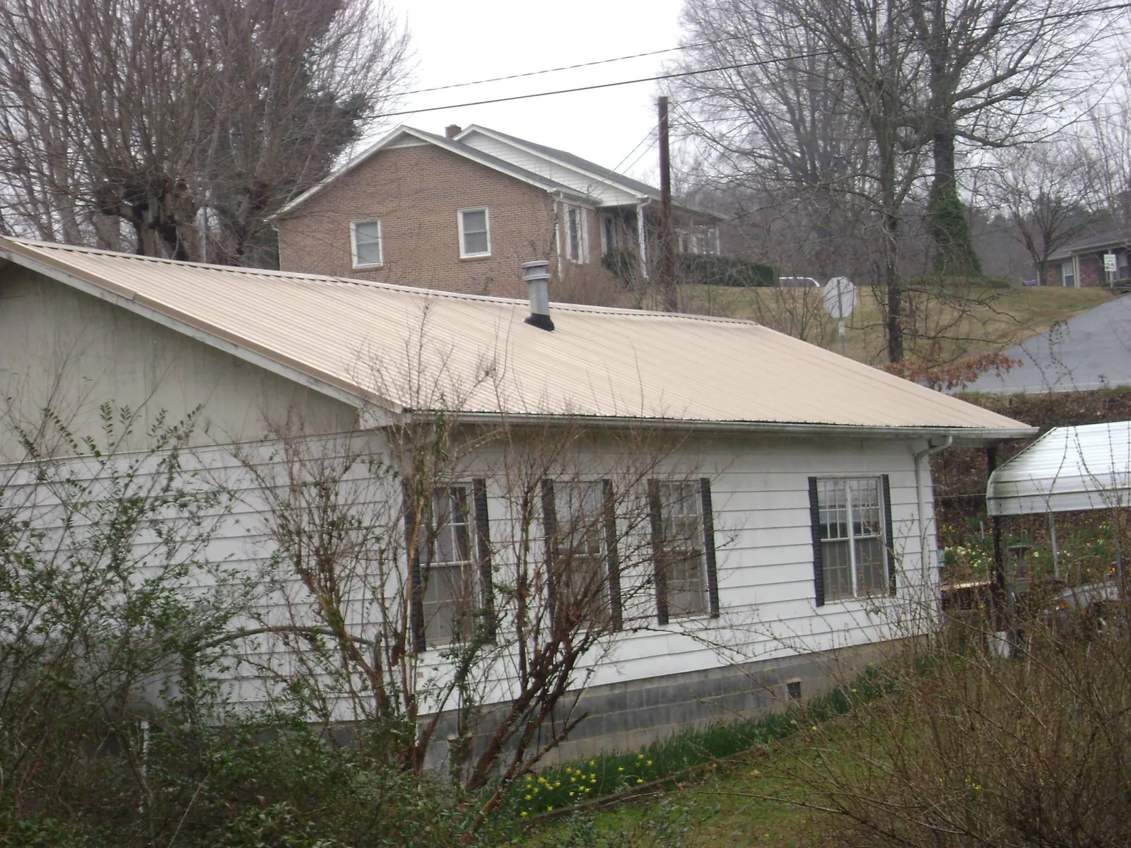Tan metal roof on a white sided house set into a hillside — Commercial Roofing by Roofing Brothers in Grand Ledge