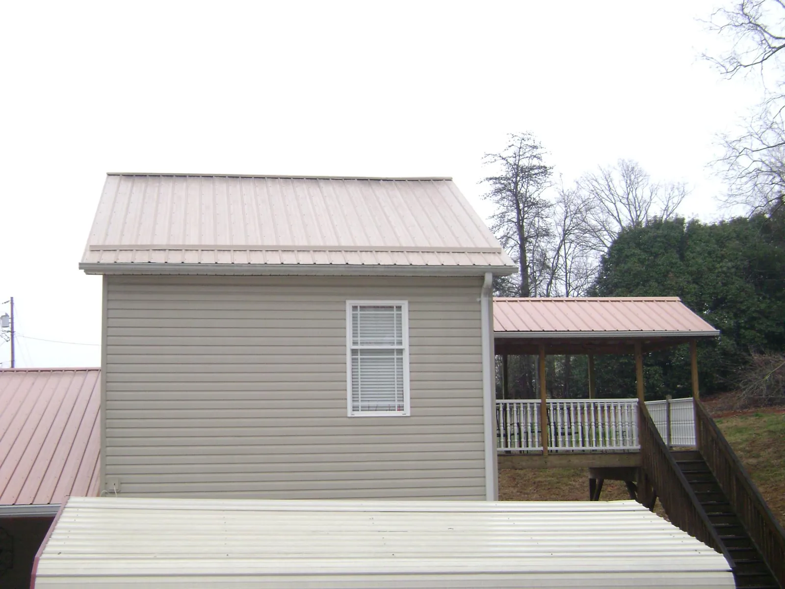 Tan metal roofs on a two story addition and attached porch, from a Roof Replacement job in Grand Ledge
